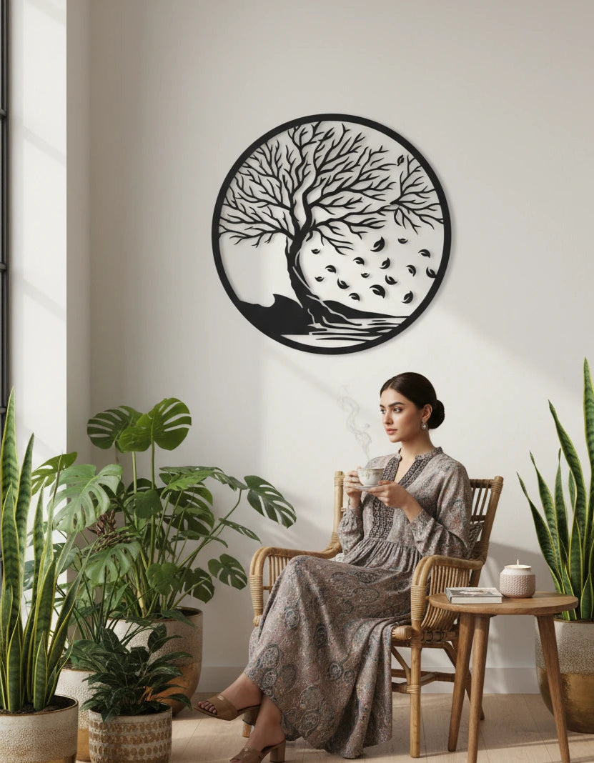 Woman sitting in a room with plants and a decorative wall piece of a tree.
