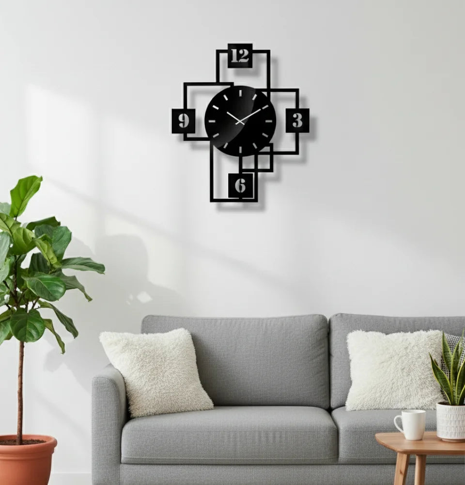 Black geometric wall clock on a white wall above a gray sofa with decorative pillows.