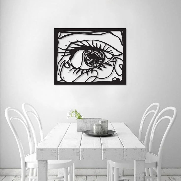 Framed artwork of a stylized eye on a wall above a dining table with chairs.
