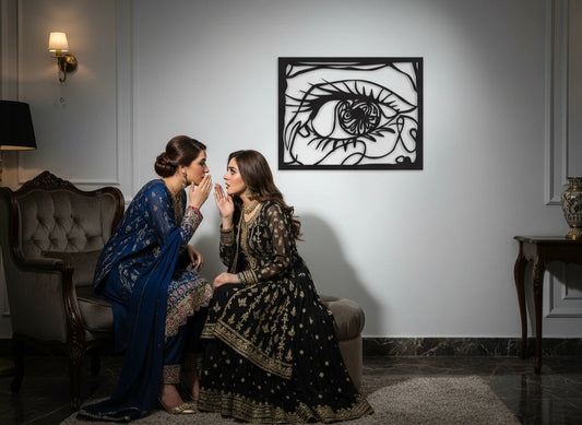 Two women in traditional attire sitting in a room with a decorative metal wall piece.
