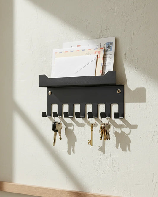Black wall-mounted key holder with keys and mail on a light-colored wall.