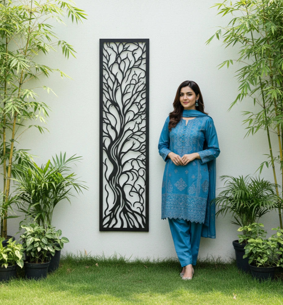 Woman in a blue outfit standing in a garden with plants and decorative metal wall panel.