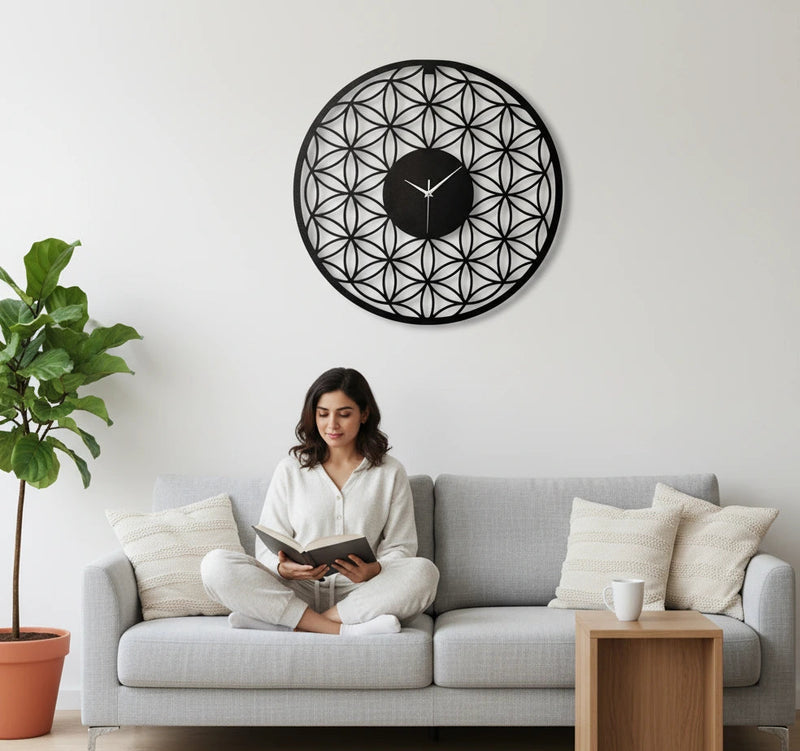 Woman reading a book on a gray sofa with a decorative wall clock in a modern living room.