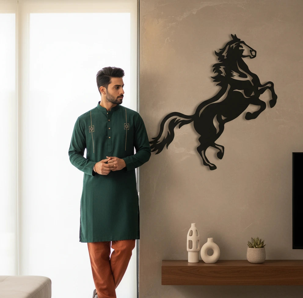 Man in a green kurta standing next to a wall with a black horse design in a modern living room.