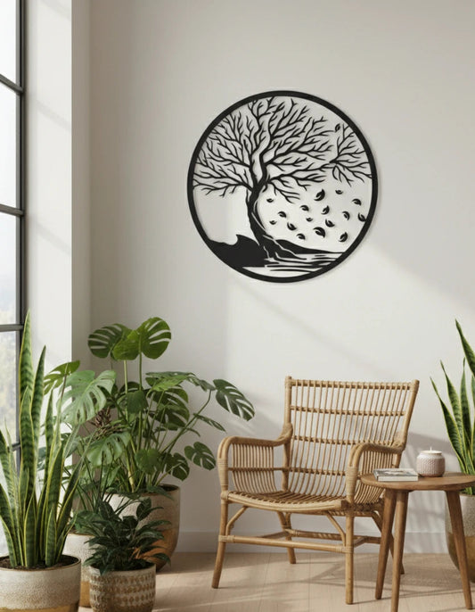 Decorative wall art of a tree with leaves on a white wall above a wicker chair and plants.