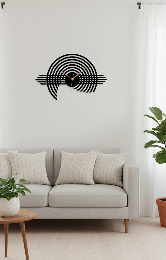Decorative wall clock on a white wall above a gray sofa with a plant in the corner.